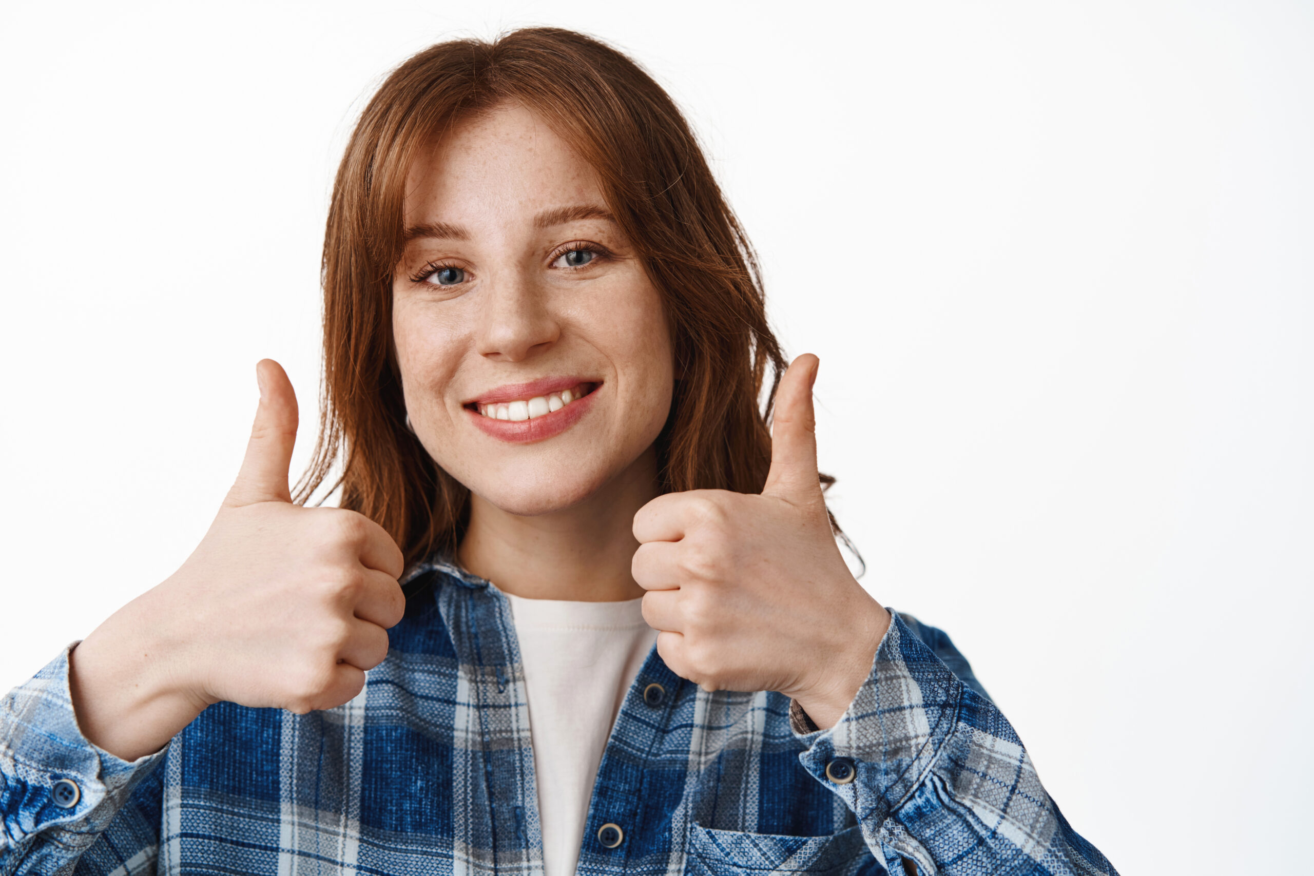 Close up portrait of beautiful ginger girl shows thumbs up, smiles white teeth, approve and agree, say yes, recommend clinic or company, satisfied with quality service, white background